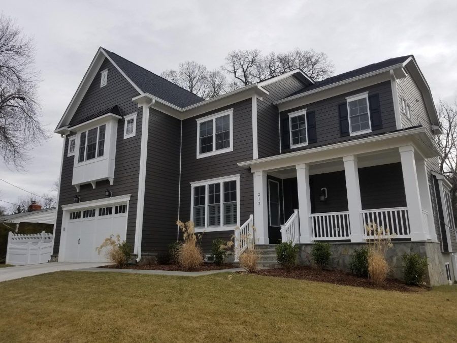 Two-story dark gray house with white trim, front porch, and attached garage on a cloudy day