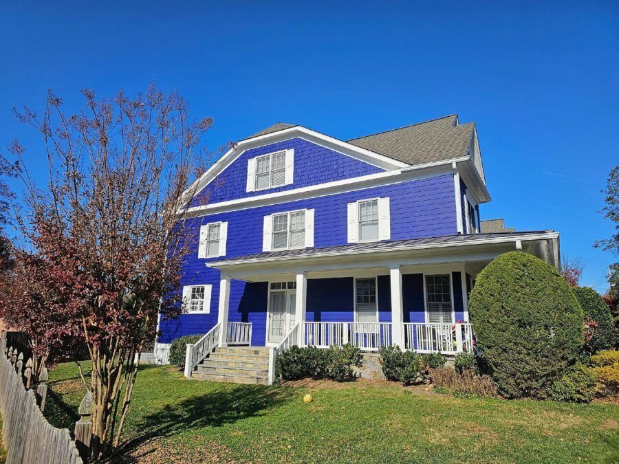 Blue two-story house with white trim, a front porch, and a green lawn under a clear blue sky