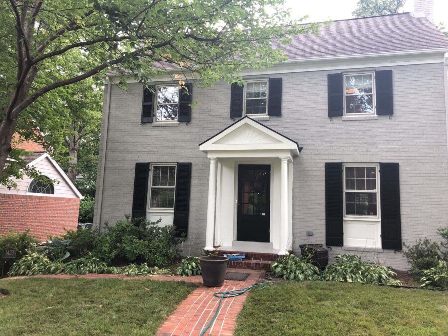 Two-story gray house with black shutters, white columns, and a brick walkway in front