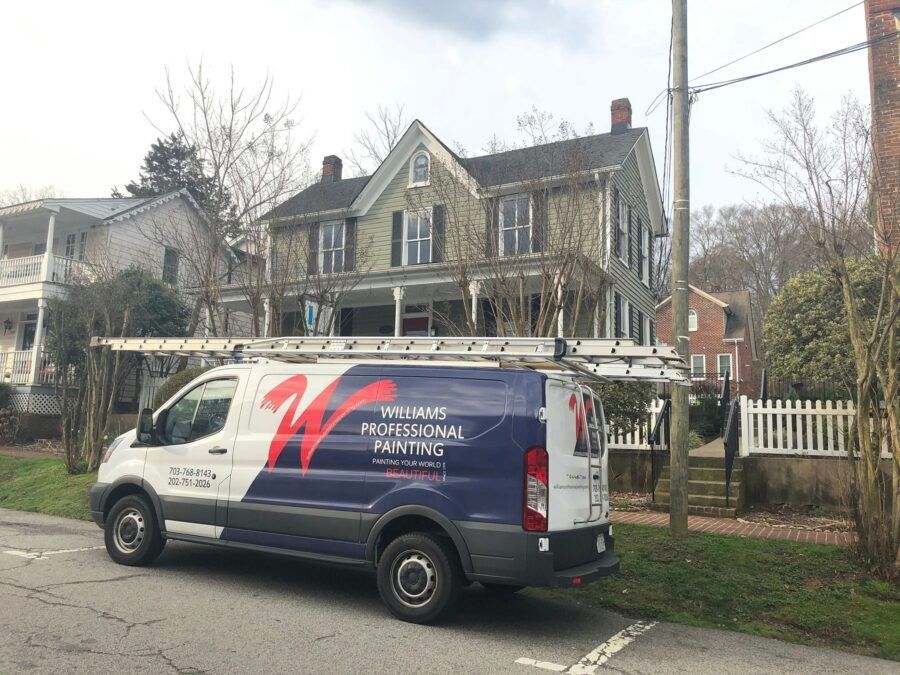 White service van parked on a residential street in front of a large house with bare trees.