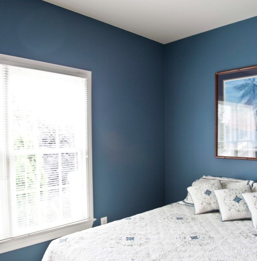 Blue bedroom with white bedspread, window blinds, and framed wall art