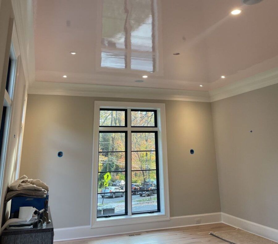 Empty beige room with white crown molding, a glossy ceiling, and a large window overlooking trees.
