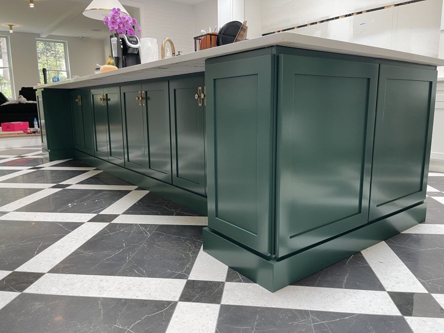 Green kitchen island with white countertop on black-and-white checkered floor in a bright room