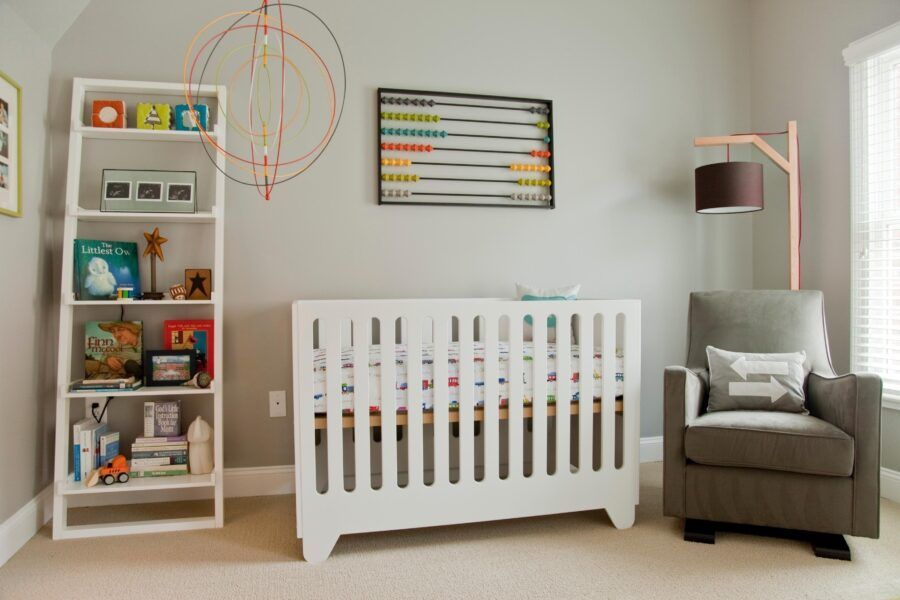 Nursery with white crib, bookshelves, gray chair, and wall decor in soft neutral tones