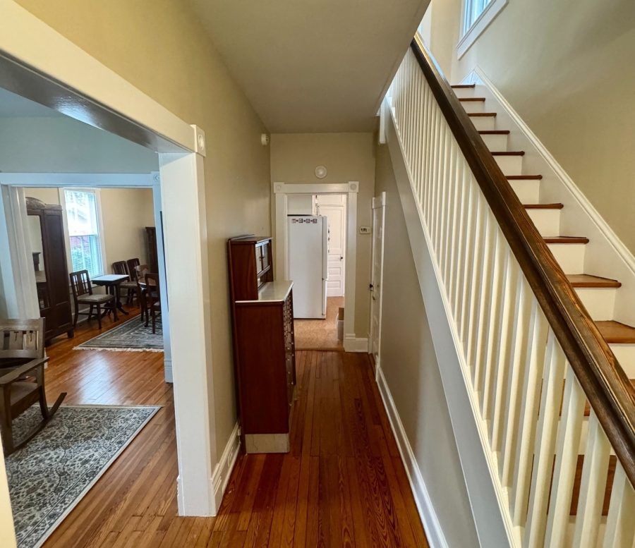 Hallway with hardwood floors and a staircase with white railing leading upstairs, open doorway to dining room