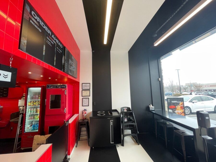 Red-and-black café interior with menu board, drink fridge, chairs, and large front windows overlooking parking lot