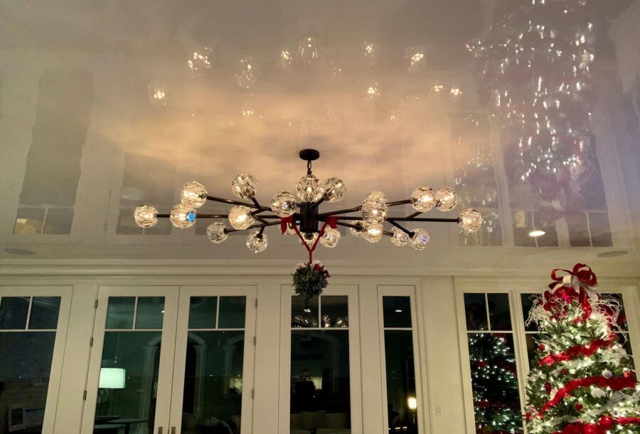 Christmas-decorated living room with a chandelier, tall windows, and a lit tree by the glass door