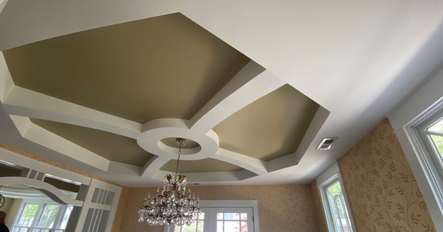 Geometric tray ceiling with beige panels, white trim, chandelier, and tall windows in a living room