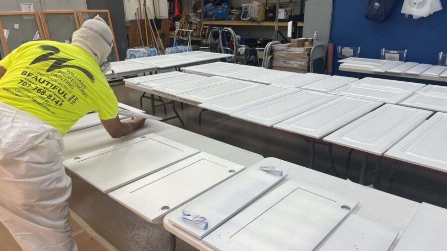 Worker in a yellow shirt inspecting white cabinet doors on an assembly line in a workshop.