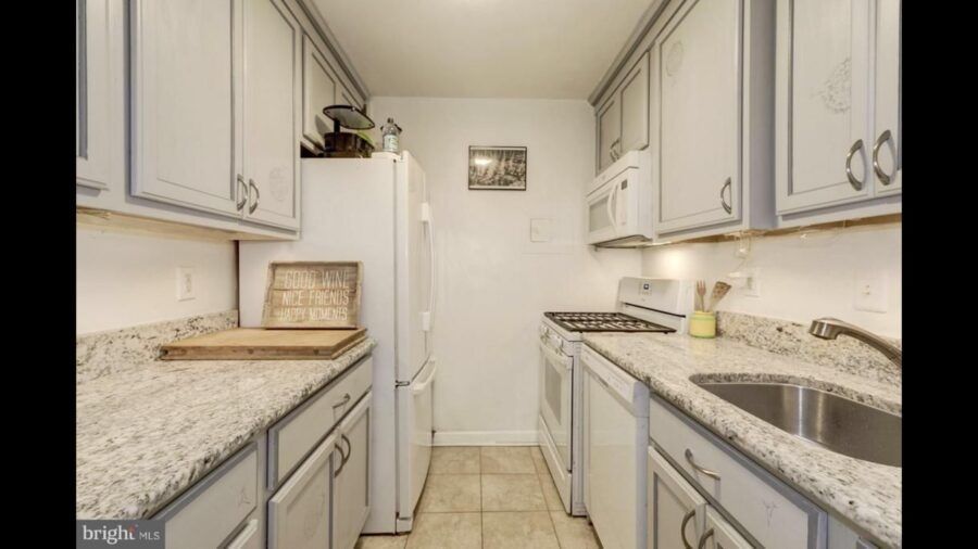 Narrow galley kitchen with light gray cabinets, granite counters, and a tile floor