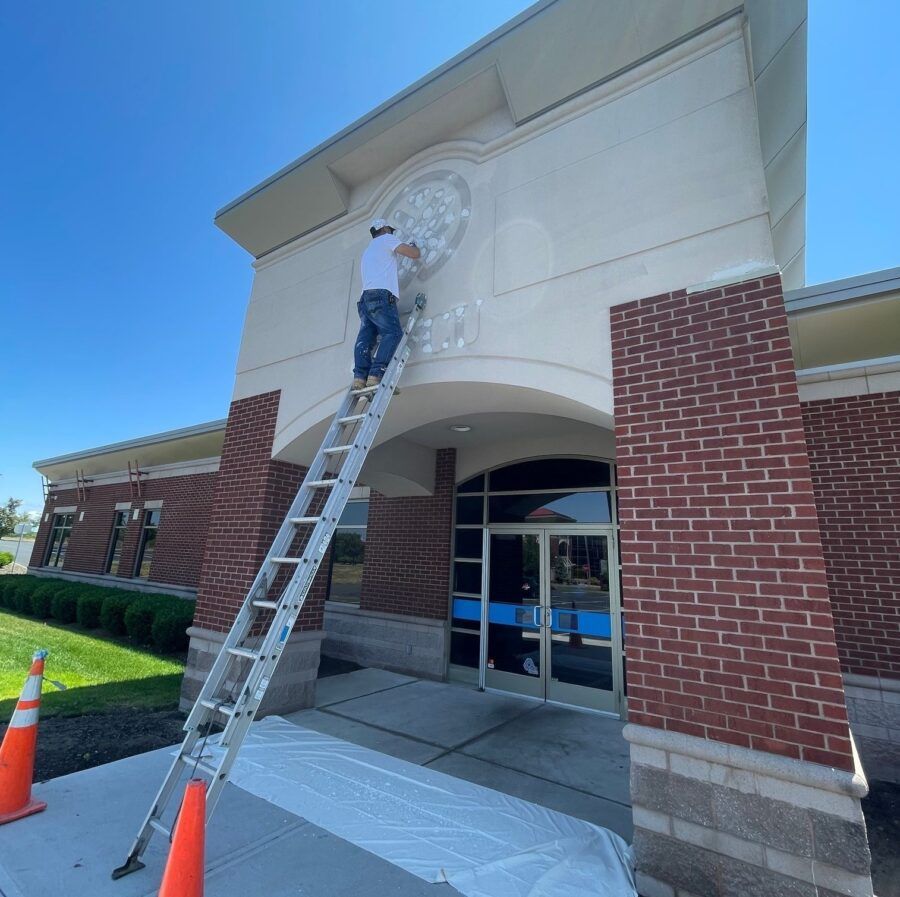 Worker on a ladder painting the facade above a brick building entrance