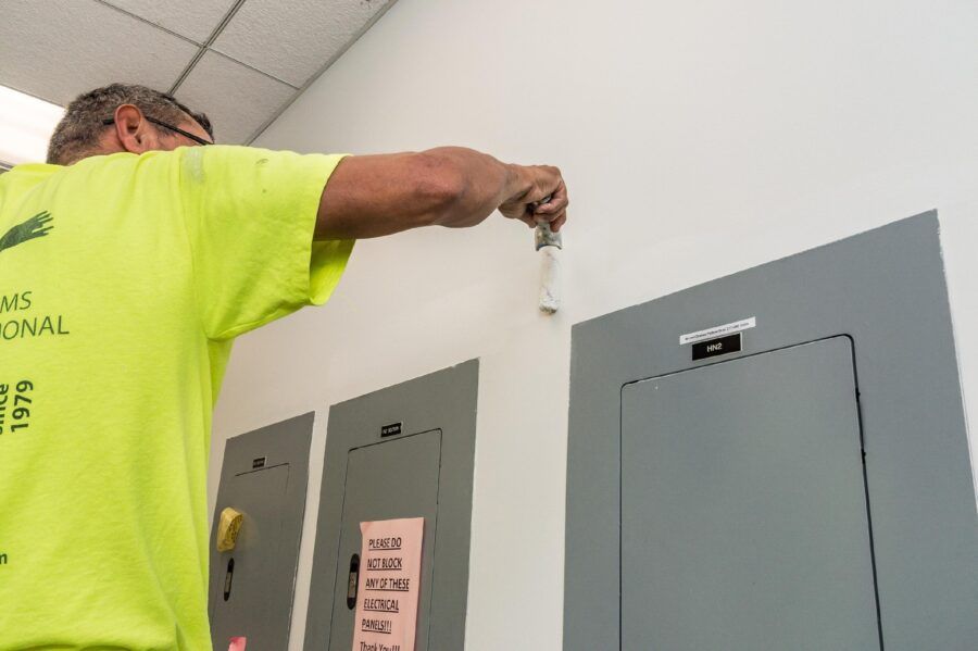 Worker in neon yellow shirt opening a gray electrical panel in a hallway