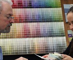 Two people discussing paint color samples in front of a wall of color swatches.