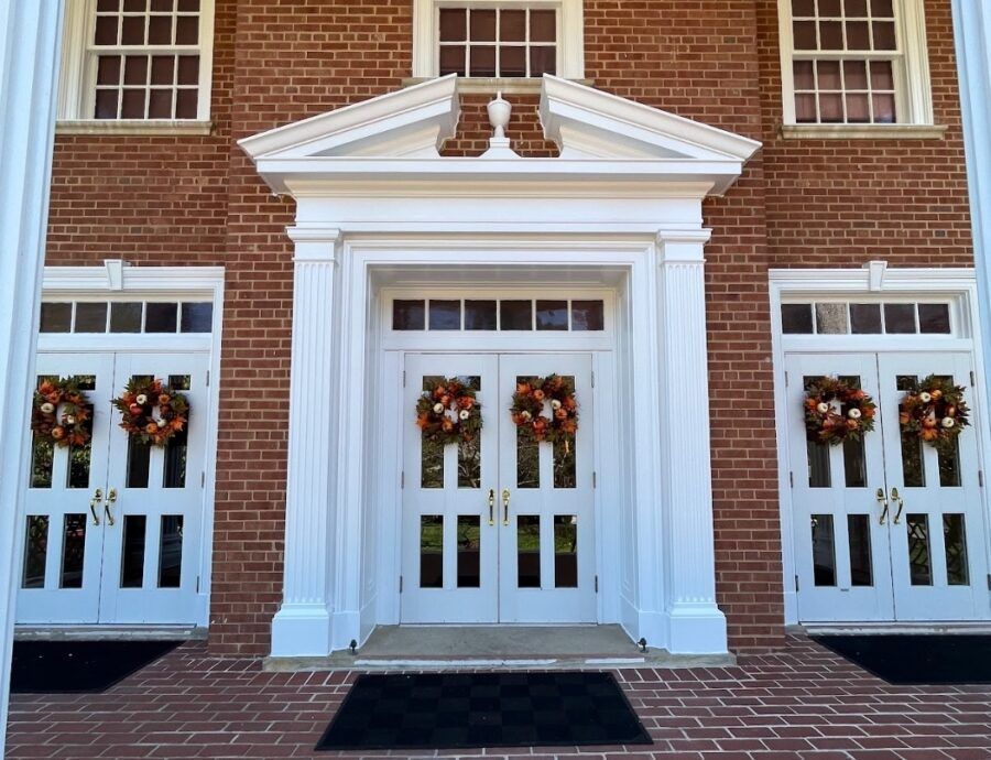 Brick building entrance with white double doors and holiday wreaths on side doors and central transom windows