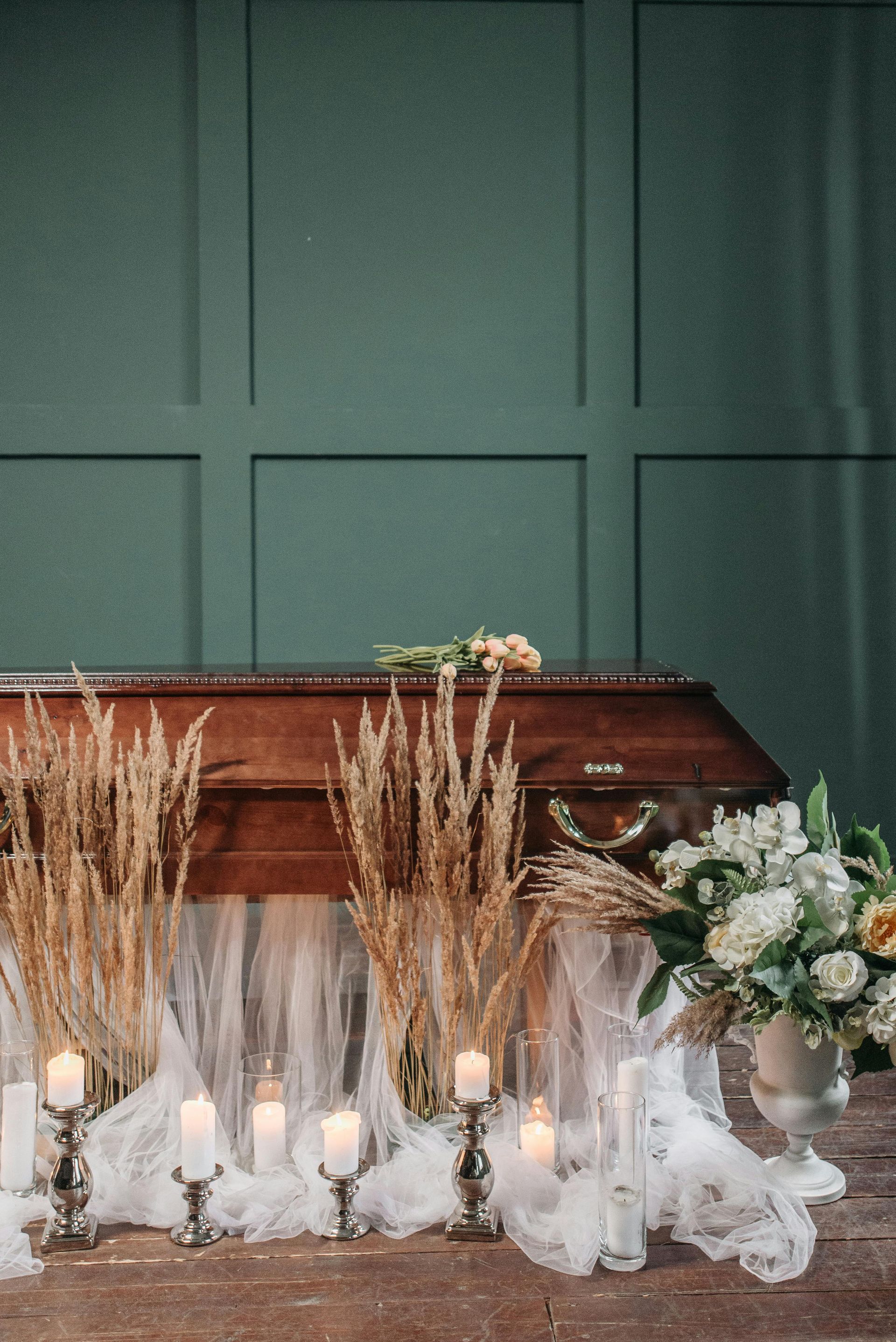 Casket surrounded by white flowers and candles against a green paneled wall