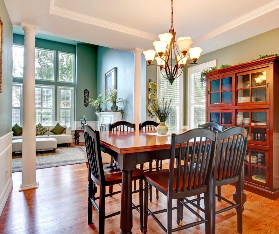 Dining room with wooden table, chairs, chandelier, and red cabinet beside a bright sitting area