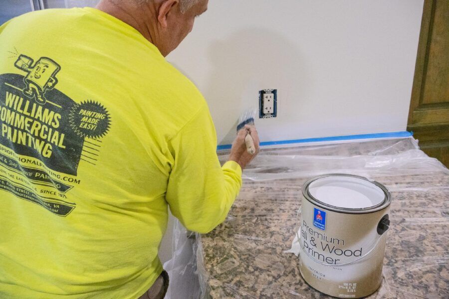 Worker painting wall trim in a room with drop cloths and a paint can nearby