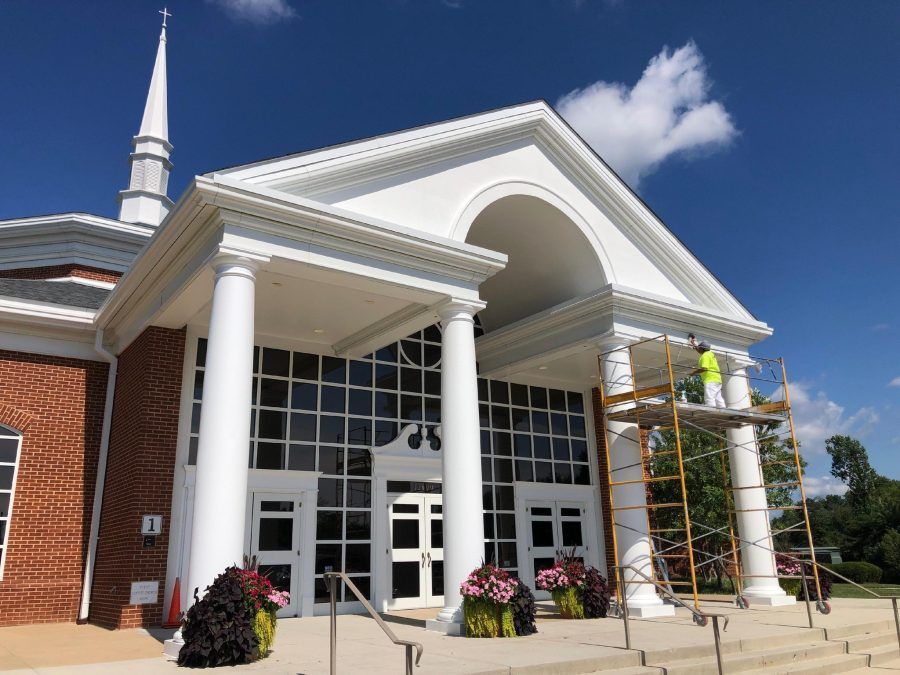 Church entrance with white columns, brick walls, arched portico, and workers on scaffolding