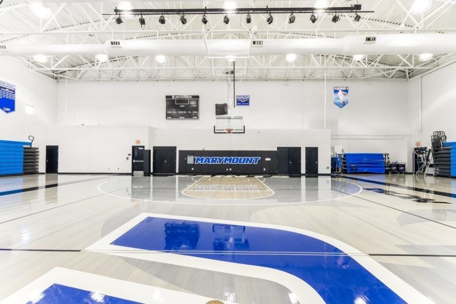 Empty indoor basketball court with blue-and-white flooring and bright overhead lights