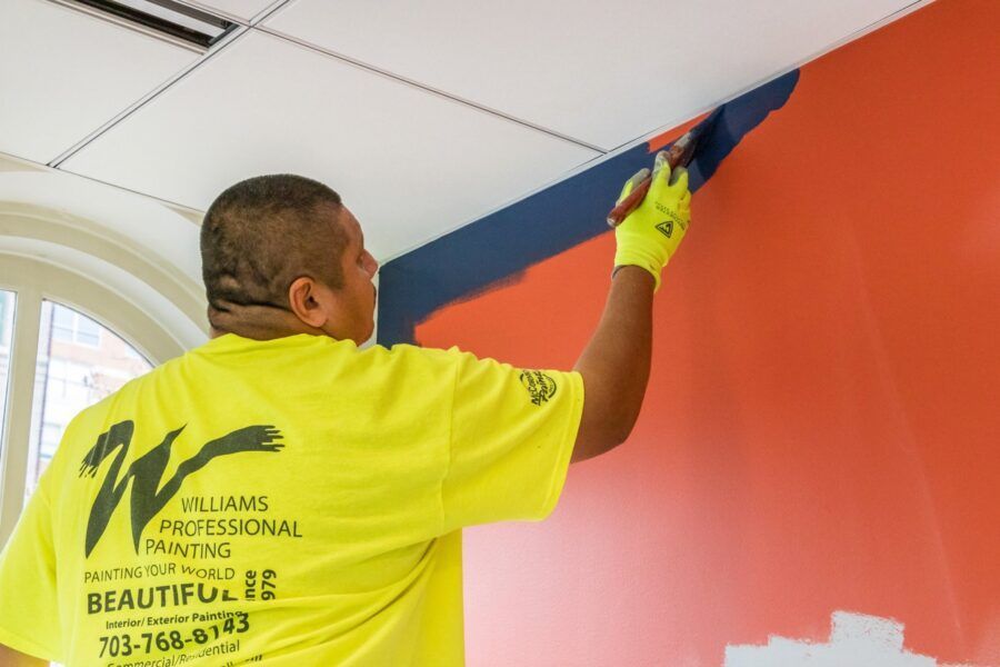 Painter in neon yellow shirt painting a wall blue in a room with a red wall and white ceiling