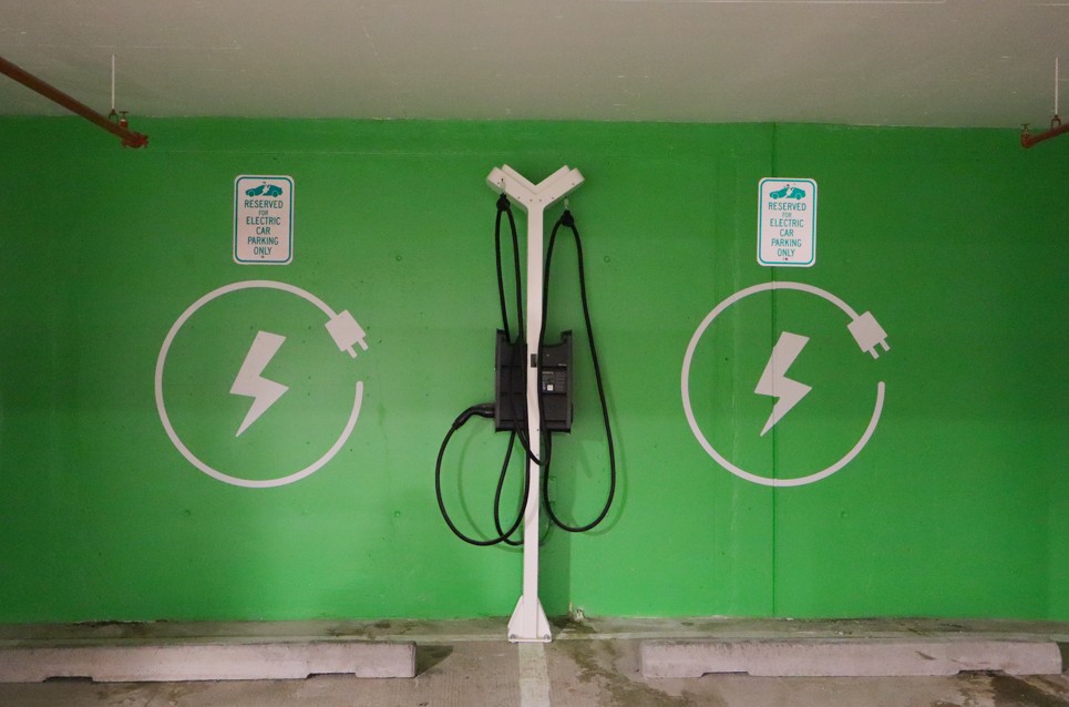 Green EV charging station with two chargers on a wall and a central cable post