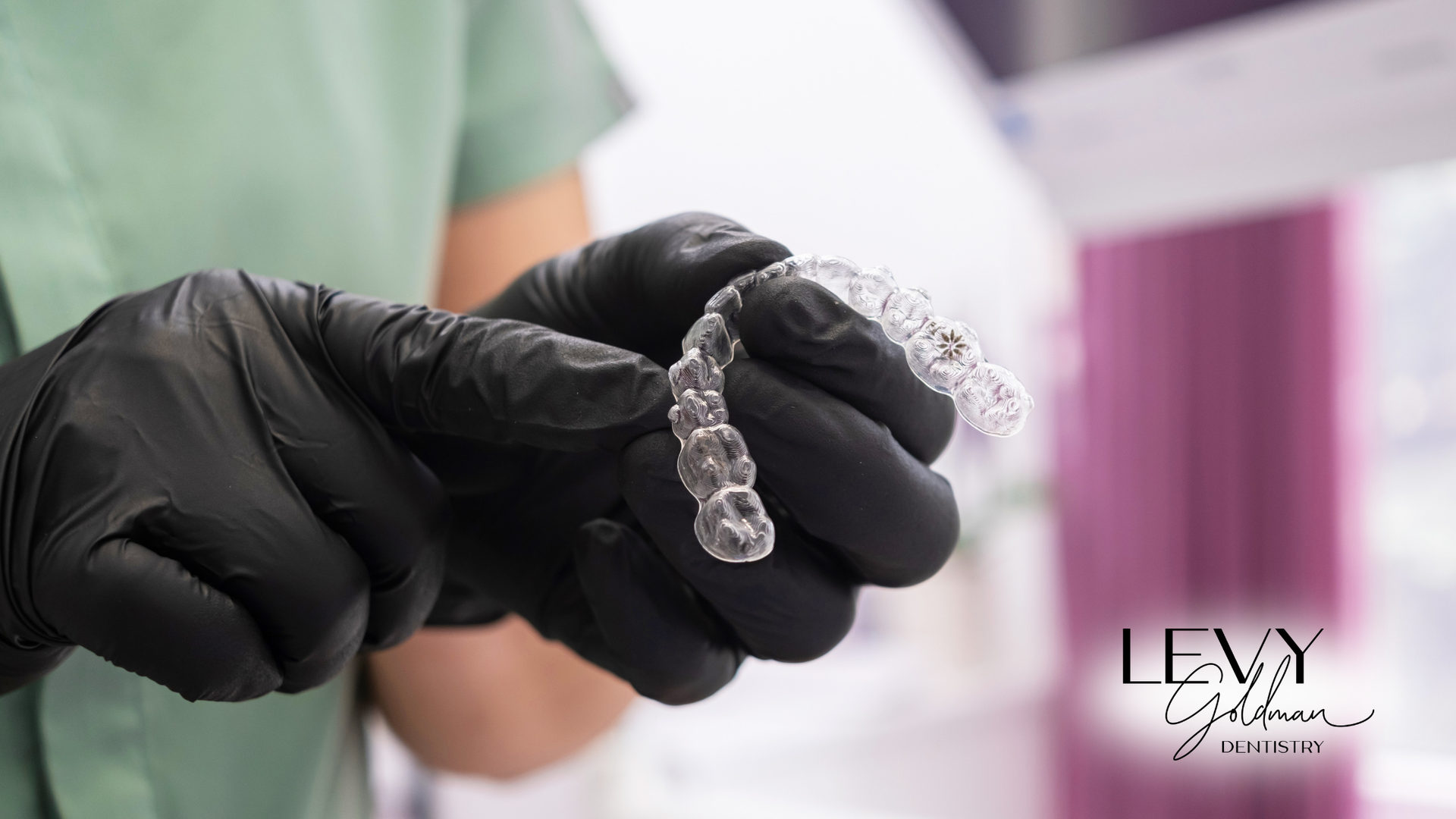 A person wearing black gloves is holding a clear brace in their hands.