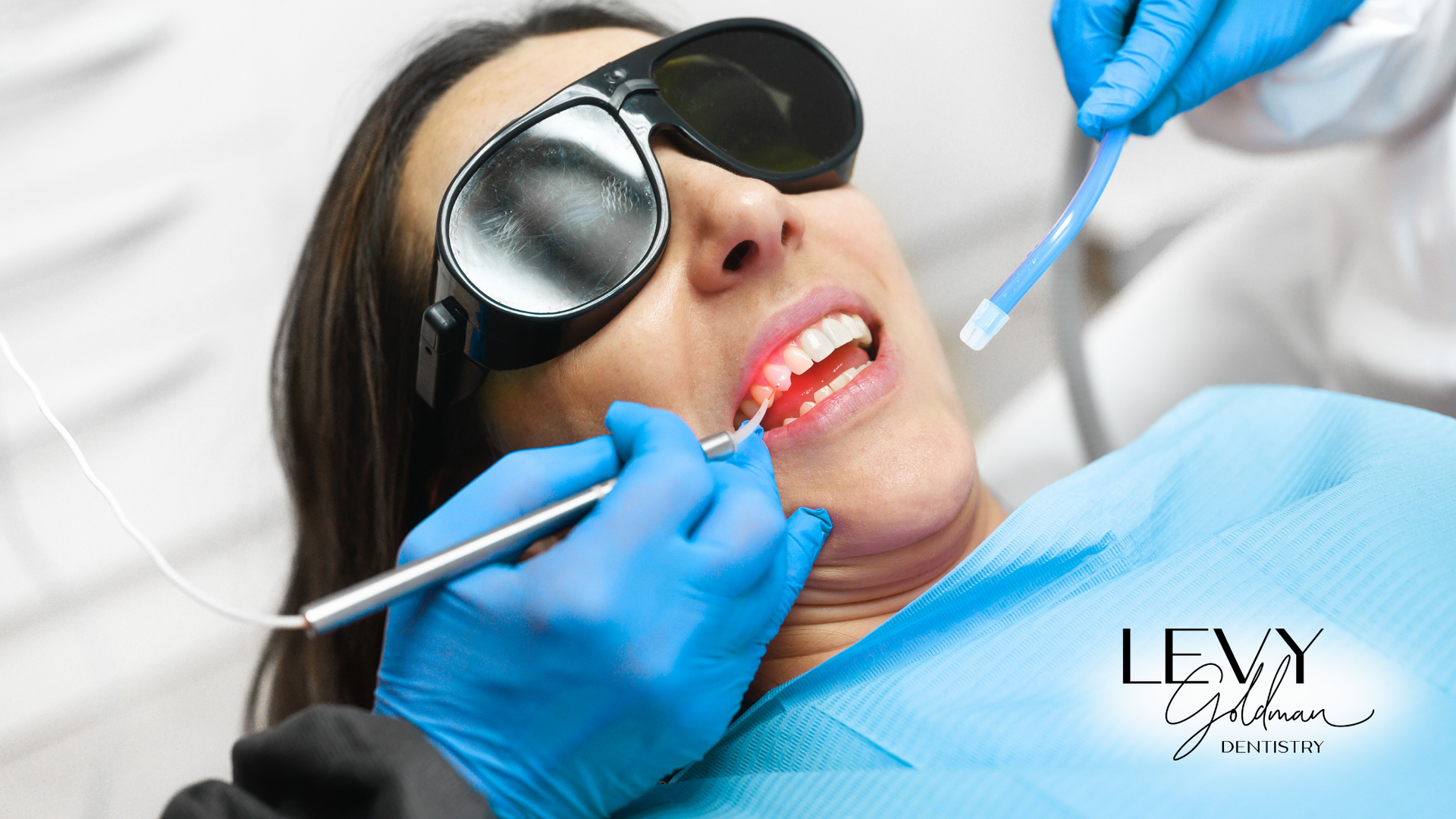 A woman wearing sunglasses is getting her teeth examined by a dentist.