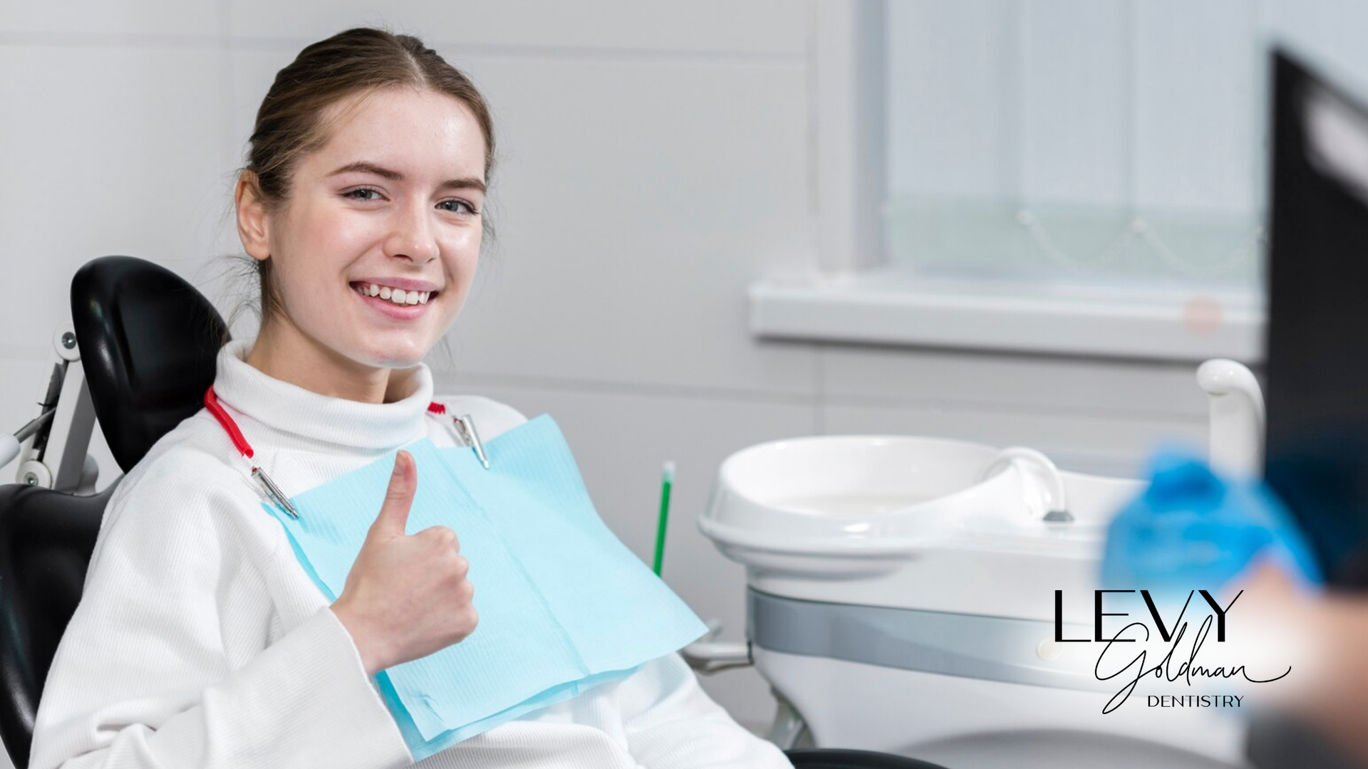 A woman is sitting in a dental chair and giving a thumbs up.