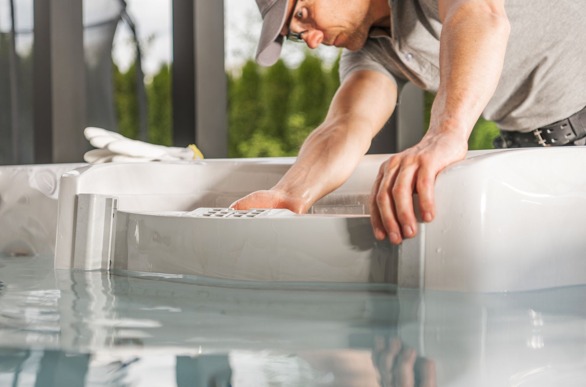 Worker cleaning a white bathtub, leaning over with hands inside in a bright bathroom