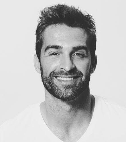A man with a beard is smiling in a black and white photo.
