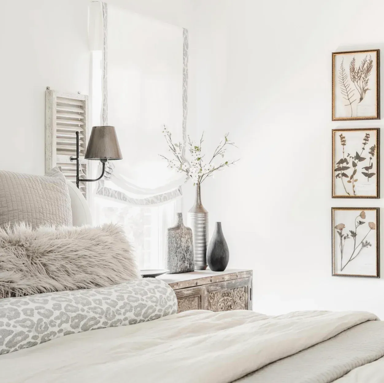 A bedroom with a bed , nightstand , vases and paintings on the wall.