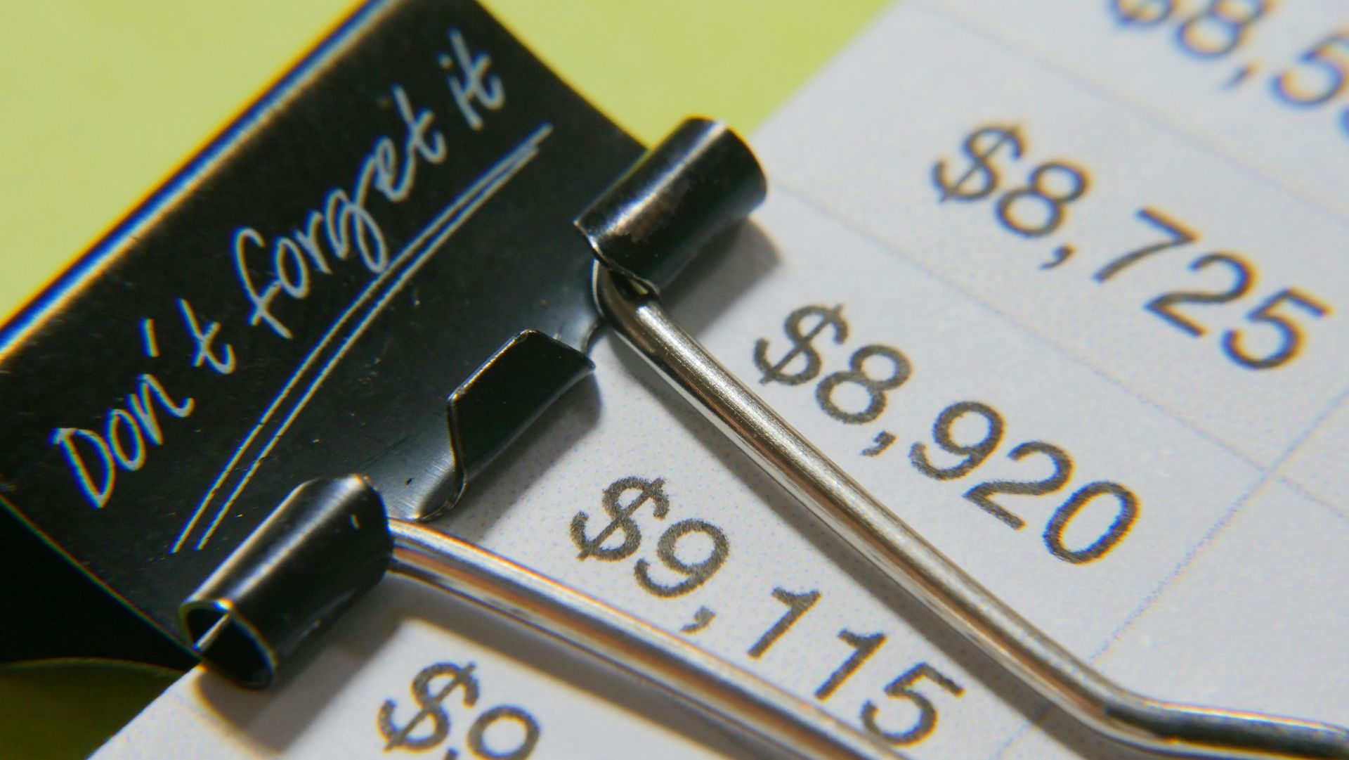 Black binder clip holding financial documents with dollar amounts. 