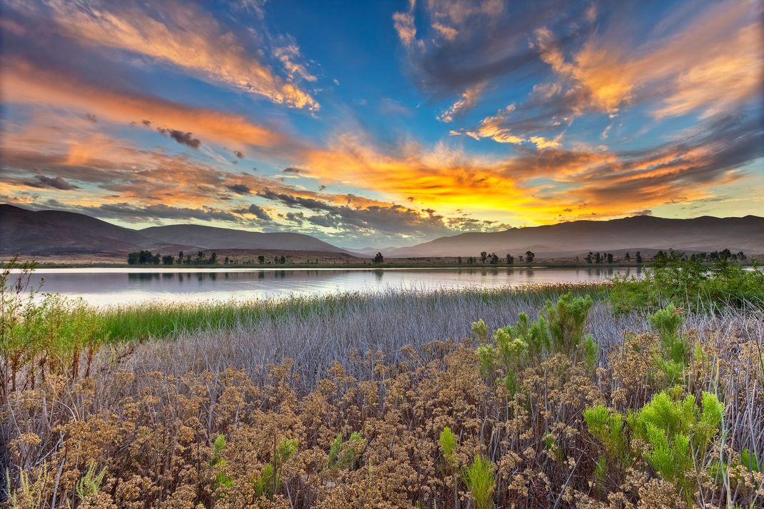 a sunset over a lake with mountains in the background