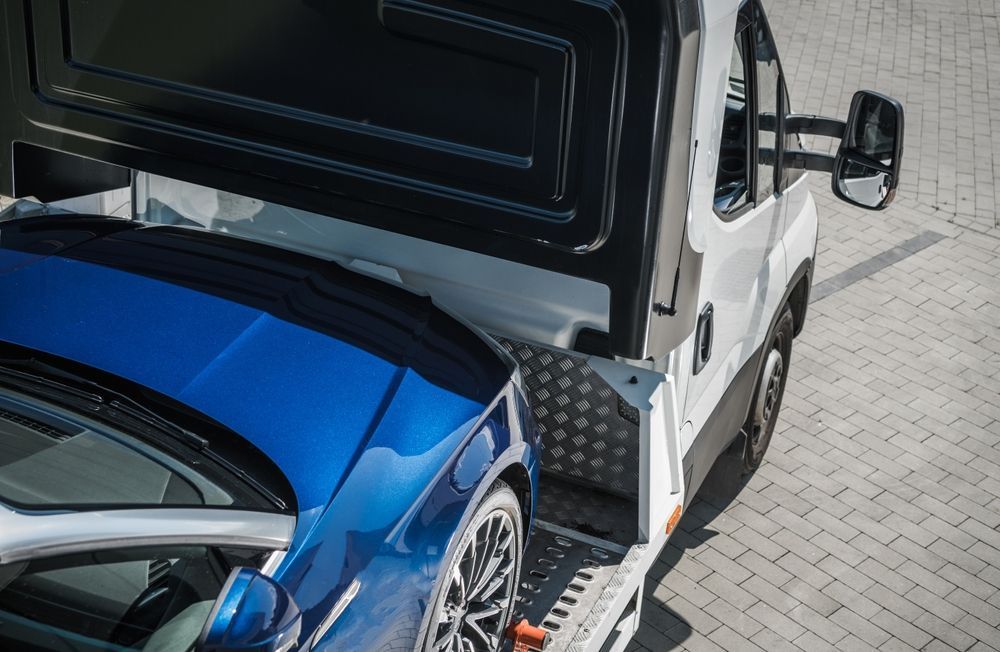 Blue car being transported on the back of a white tow truck on a brick surface.