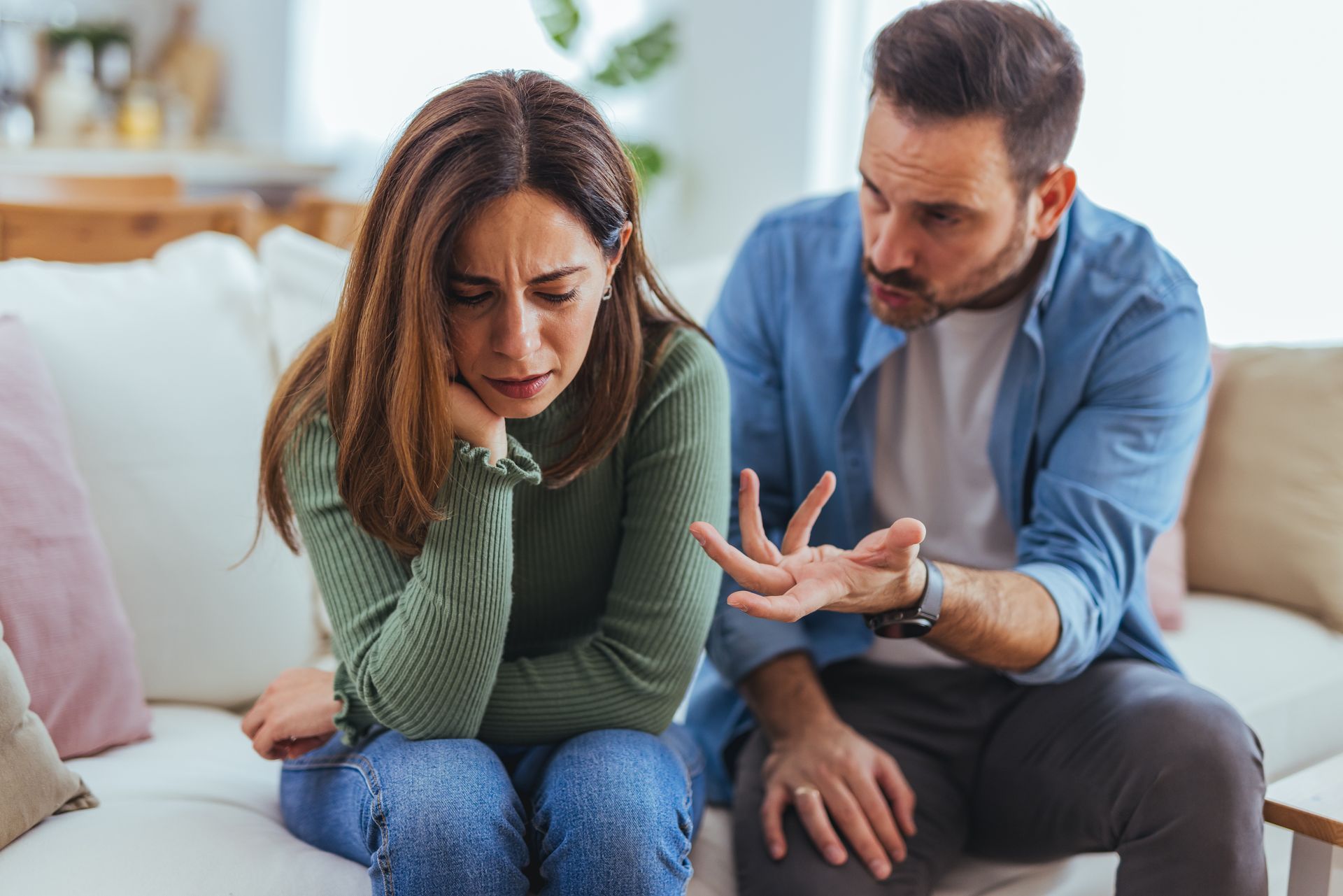 Crying woman on couch while man beside her gestures during a tense conversation