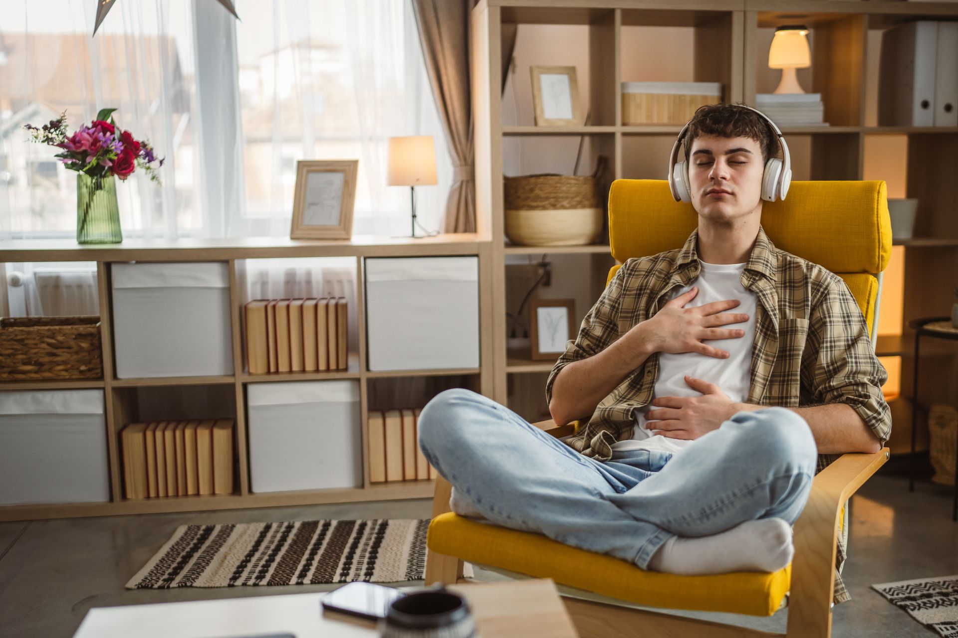 Two people seated on a sofa, one speaking while the other listens in a counseling setting Man sitting cross-legged in a yellow chair, holding a mug in a cozy living room with shelves and warm light