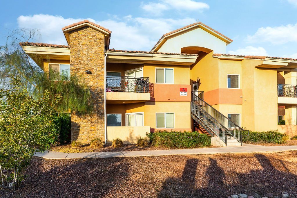 Two-story apartment building with stucco exterior, tan and orange, with brown stone accents and a stairway.