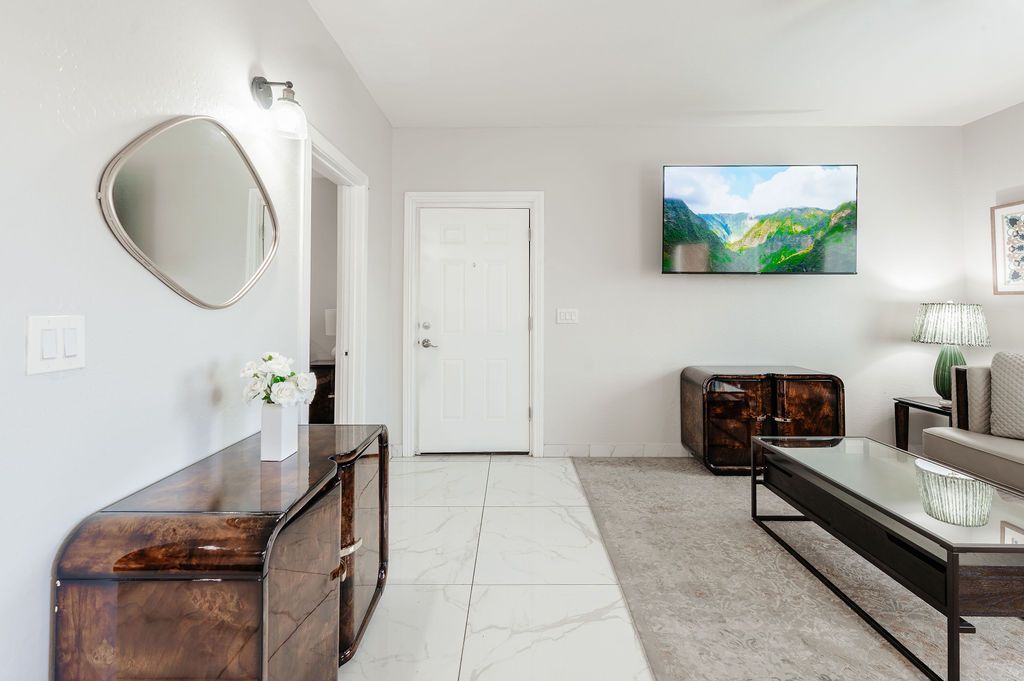 Spacious, light-filled living area with hardwood furniture, large mirror, and television above a cabinet.