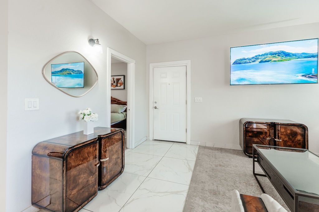 Living room with a mirror, furniture, TV, and an open doorway. Gray and white color scheme.