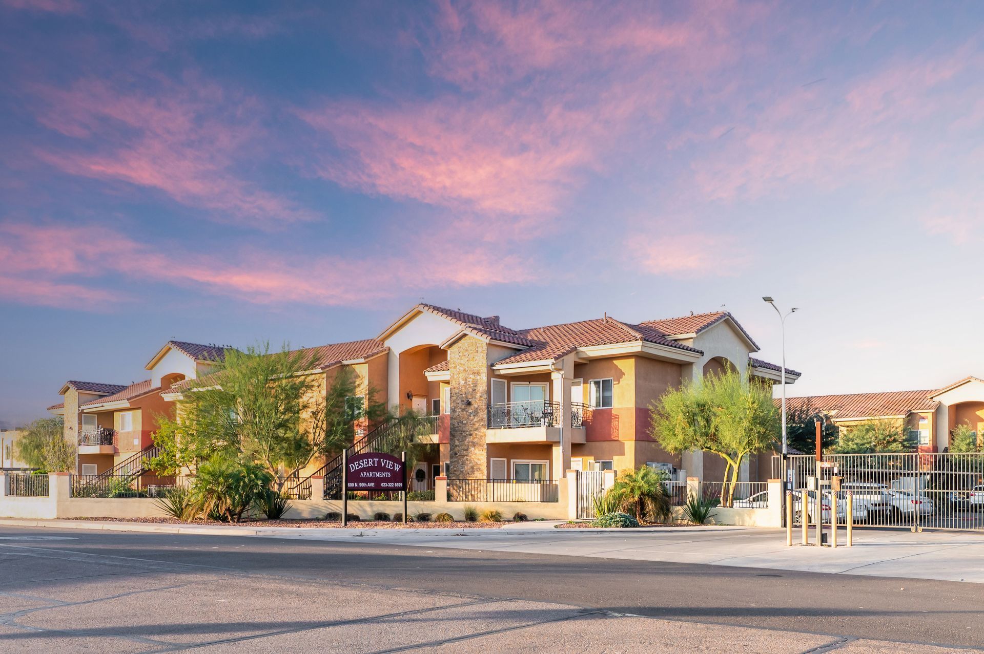Multi-story building with tan stucco and tile roof at sunset; sign reads 