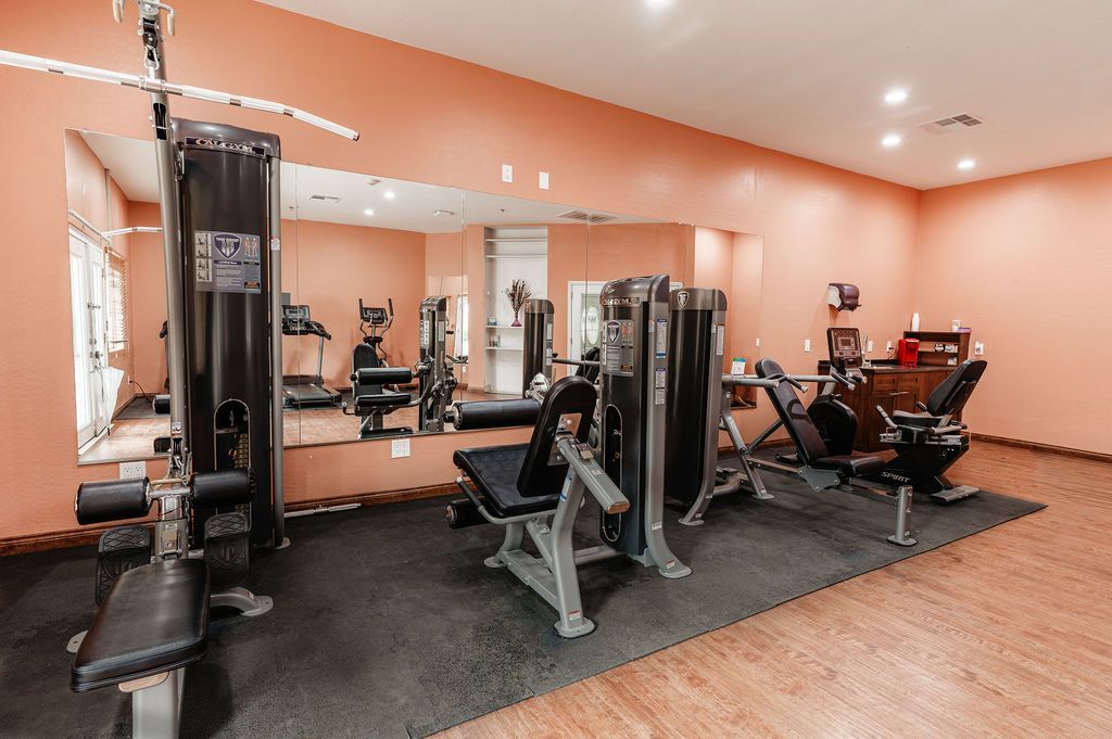Gym with weight machines and treadmills on a dark floor with a large mirror.