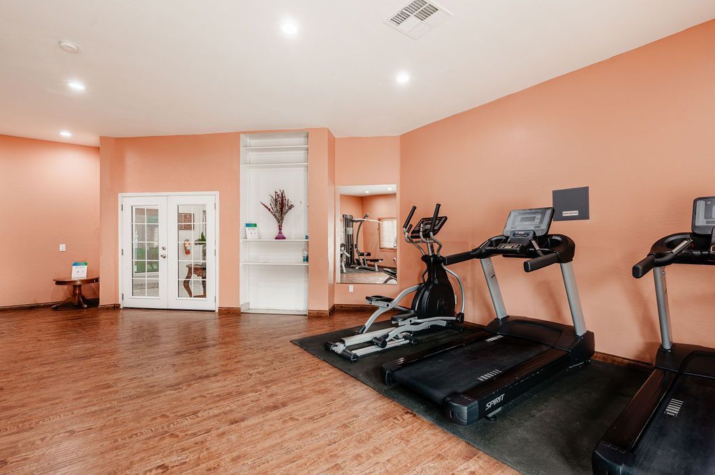 Gym interior with treadmills, exercise bike, and mirrored wall. Pink walls and hardwood floor.