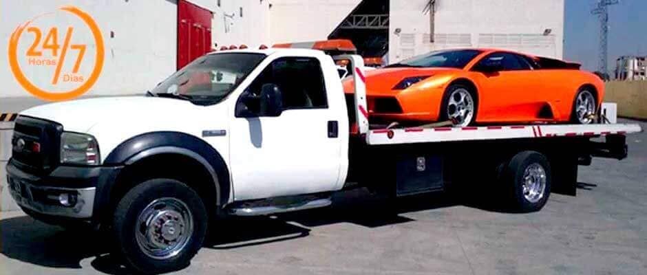 Una grúa blanca con un auto deportivo naranja en la parte trasera.