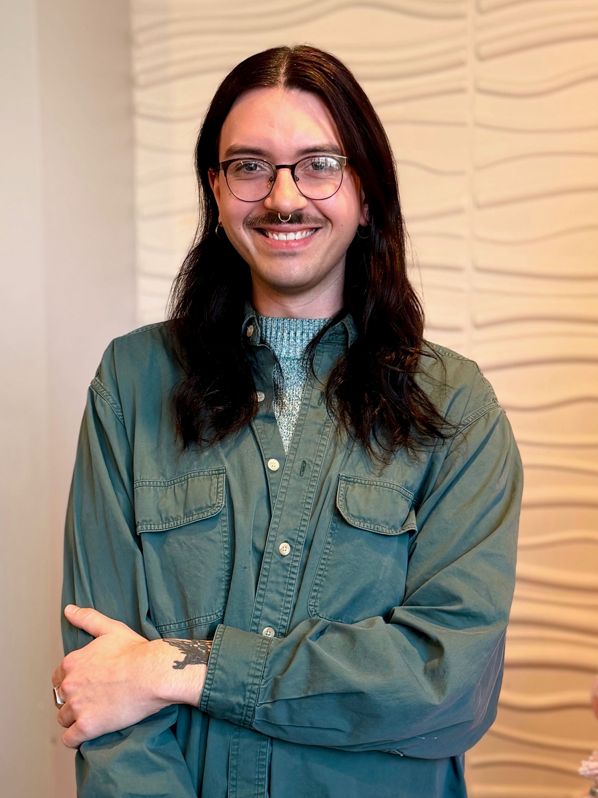A man with long hair and glasses is sitting in a chair and smiling.