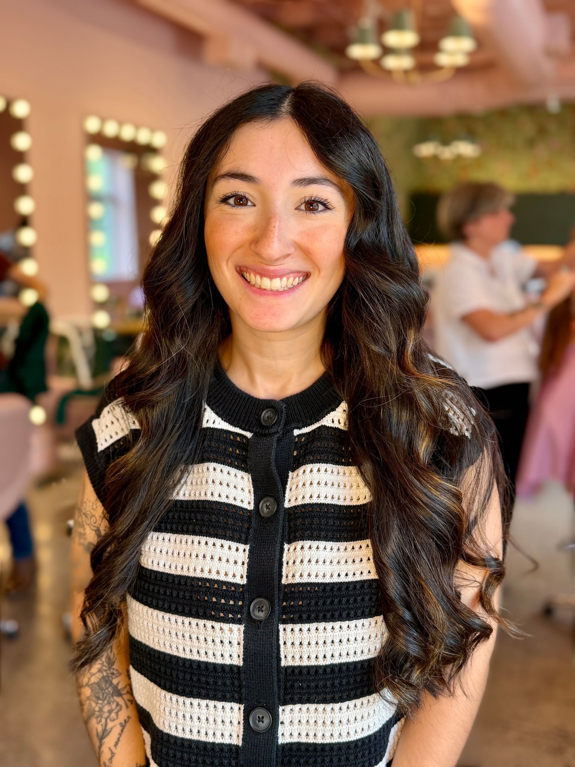 Close-up of a stylist’s hands using silver scissors and a green comb to trim straight, dark hair.