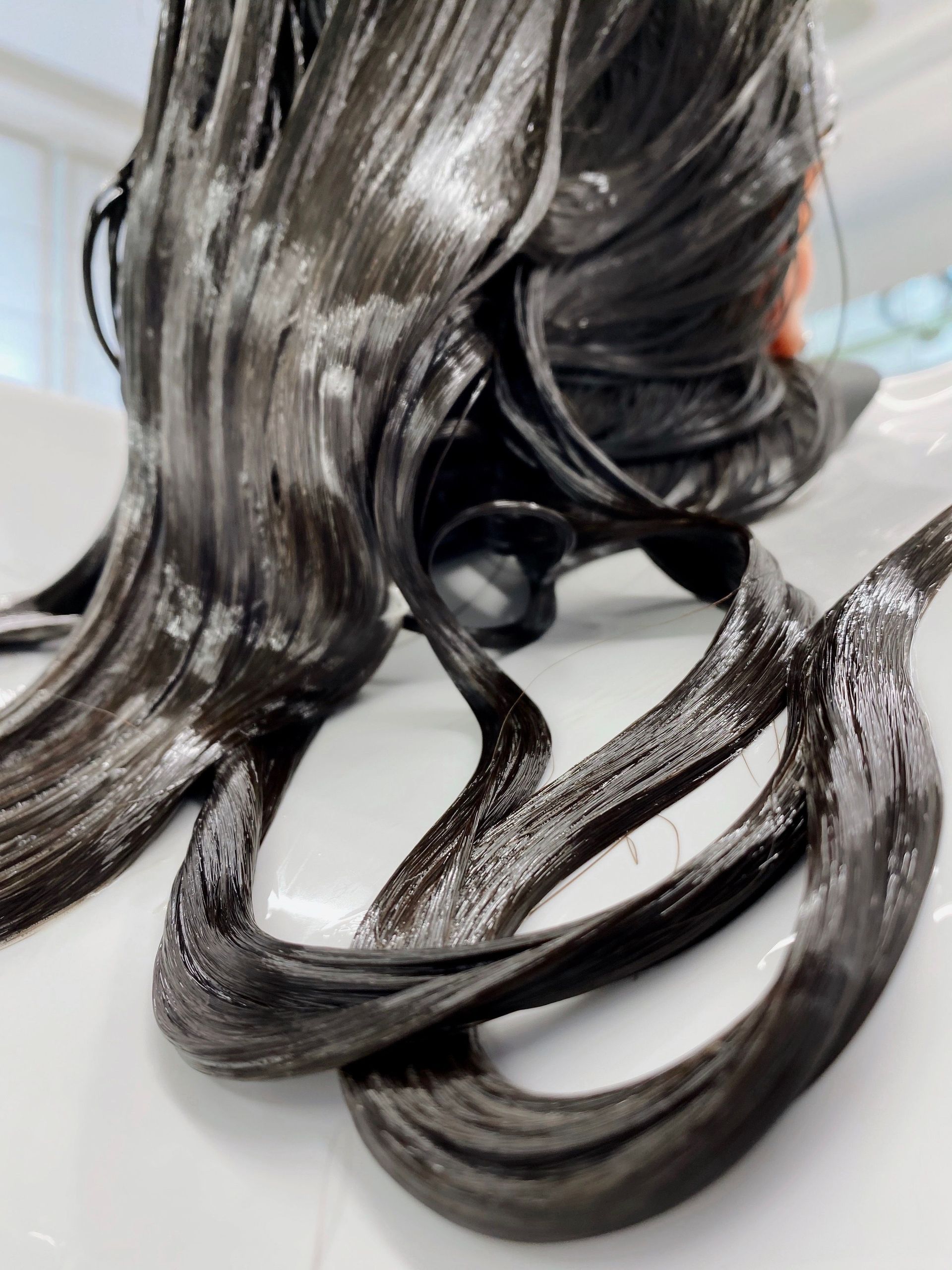 Close-up of shiny black wet hair strands draped over a white surface
