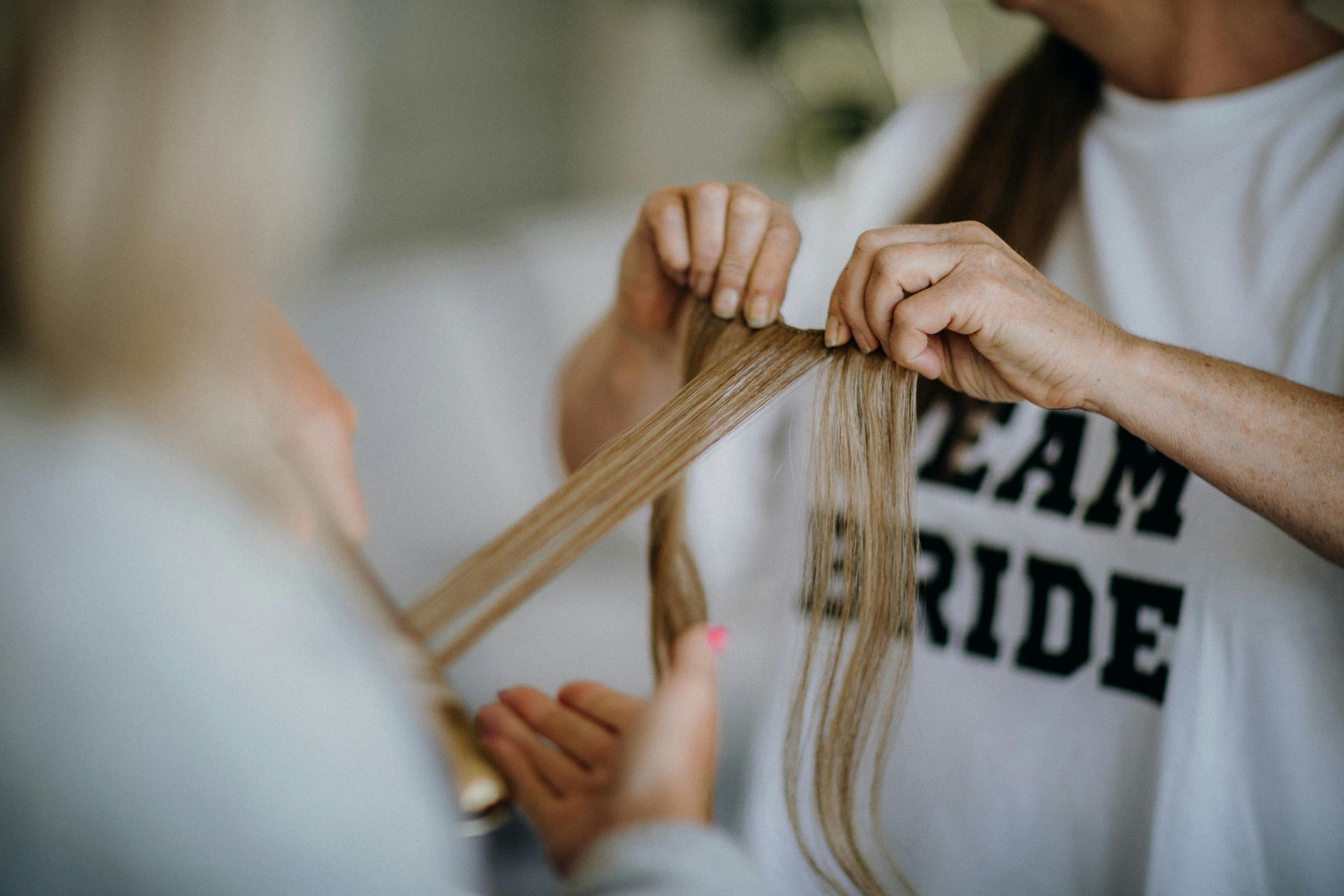 Hands styling long blonde hair on a person wearing a white “BRIDE” shirt.
