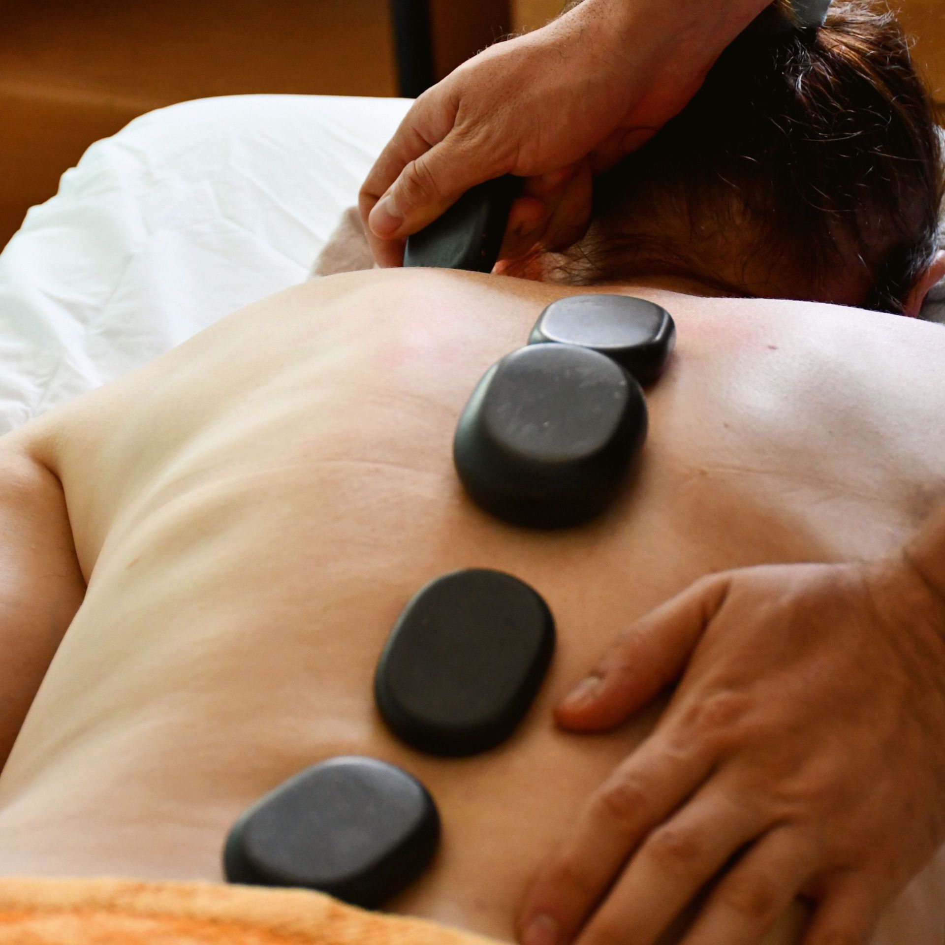 Hot stone massage on a person’s back with hands placing smooth black stones