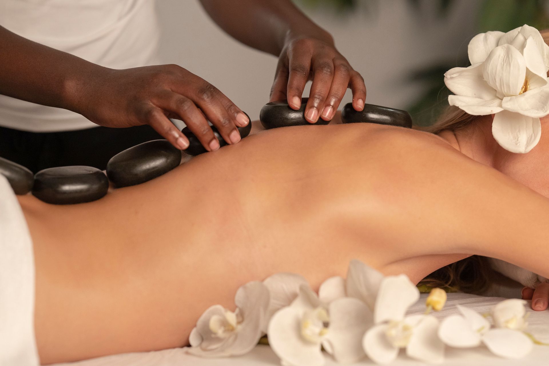 Hot stone massage on a person’s back with white flowers nearby
