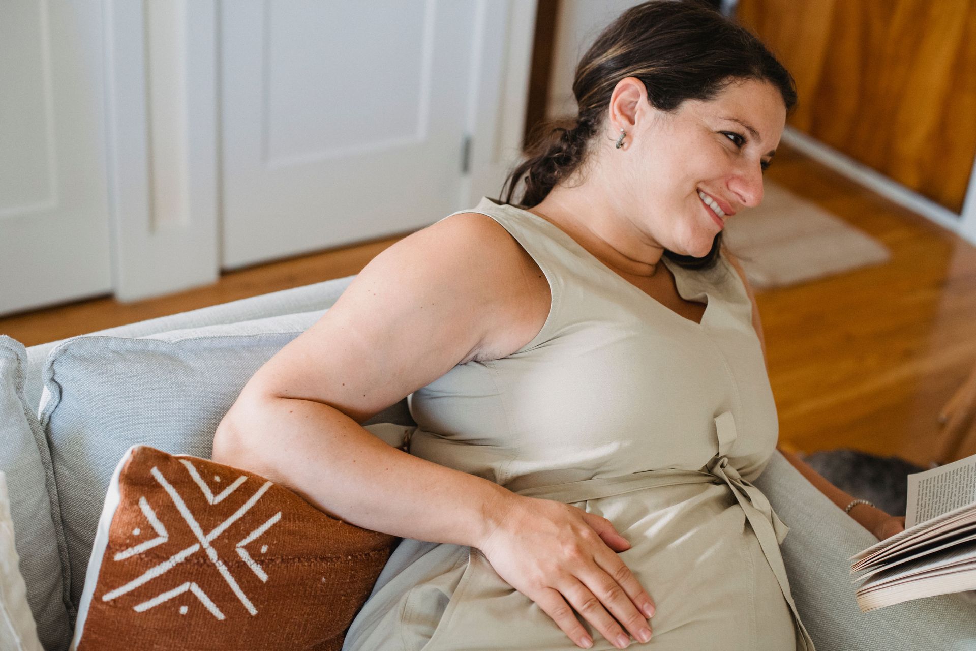 Pregnant woman reclining on a couch and smiling at a laptop in a bright living room
